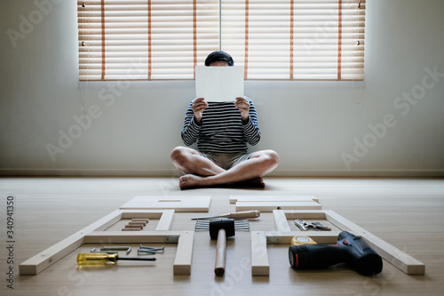 Young asian man self assembly wooden furniture and read blank white paper to put instruction photo