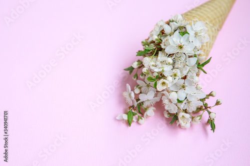 Fototapeta Naklejka Na Ścianę i Meble -  Ice cream cone with white flowers on a pink background. Spring concept. Floral background. Flat lay. Space for text
