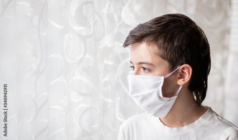 Portrait of child in a protective white mask near the window. House pandemic period. Concept of the fight against coronavirus covid-19. Portrait of child in a protective white mask near the window. House pandemic period. Concept of the fight against coronavirus covid-19.