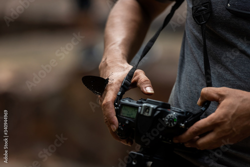 Close up hand and butterfly. Professional photographer man holding camera for taking butterfly in the green jungle rain forest nature. Travel and Vacations Concept