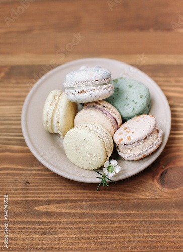 Colorful homemade macarons are lying on the beige plate on the brown wooden background. Pattern.