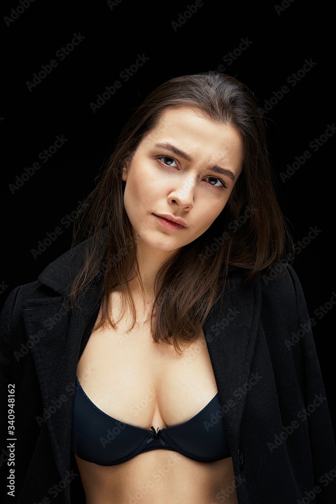Naklejka premium Dramatic portrait of a beautiful lonely girl isolated on a dark background. Young brunette woman with healthy clean skin. People, emotions, stress and health care concept.