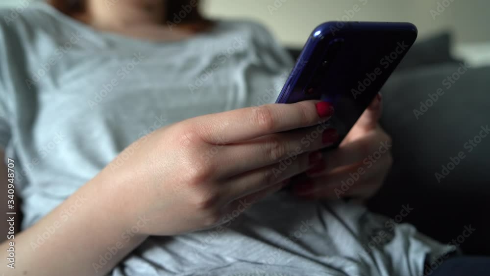 Close up on midsection of unknown female woman girl sitting on the sofa bad at home hands holding and using mobile smartphone phone scrolling browsing internet or checking social network in day Close up on midsection of unknown female woman girl sitting on the sofa bad at home hands holding and using mobile smartphone phone scrolling browsing internet or checking social network in day
