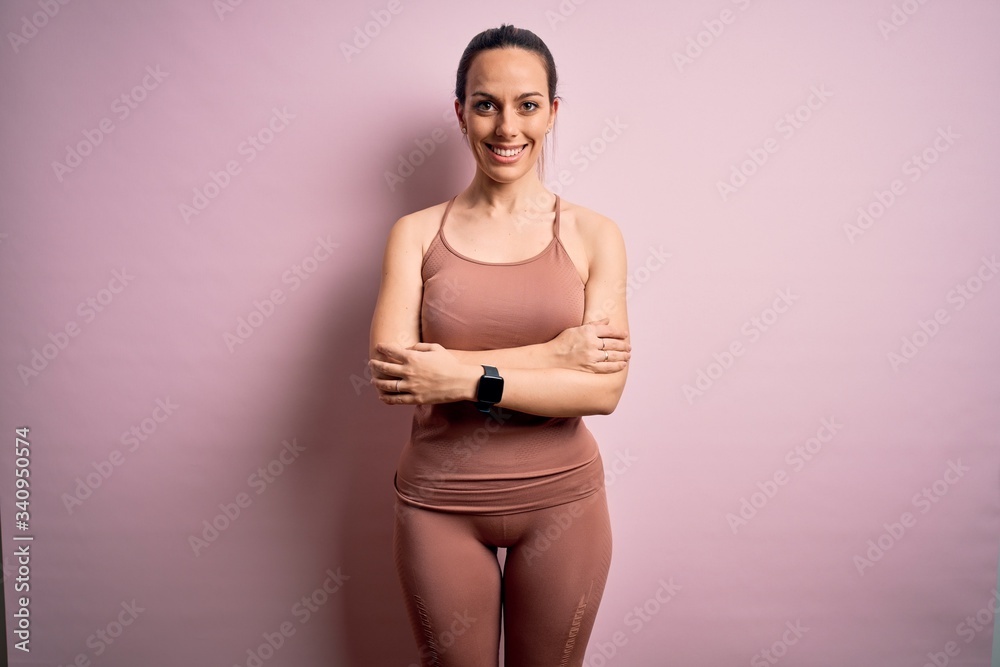 Young blonde fitness woman wearing sport workout clothes over pink isolated background happy face smiling with crossed arms looking at the camera. Positive person. Young blonde fitness woman wearing sport workout clothes over pink isolated background happy face smiling with crossed arms looking at the camera. Positive person.