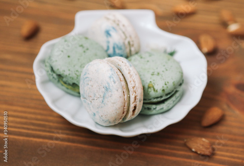 Home made green and white macarons are lying on the white plate on wooden brown background