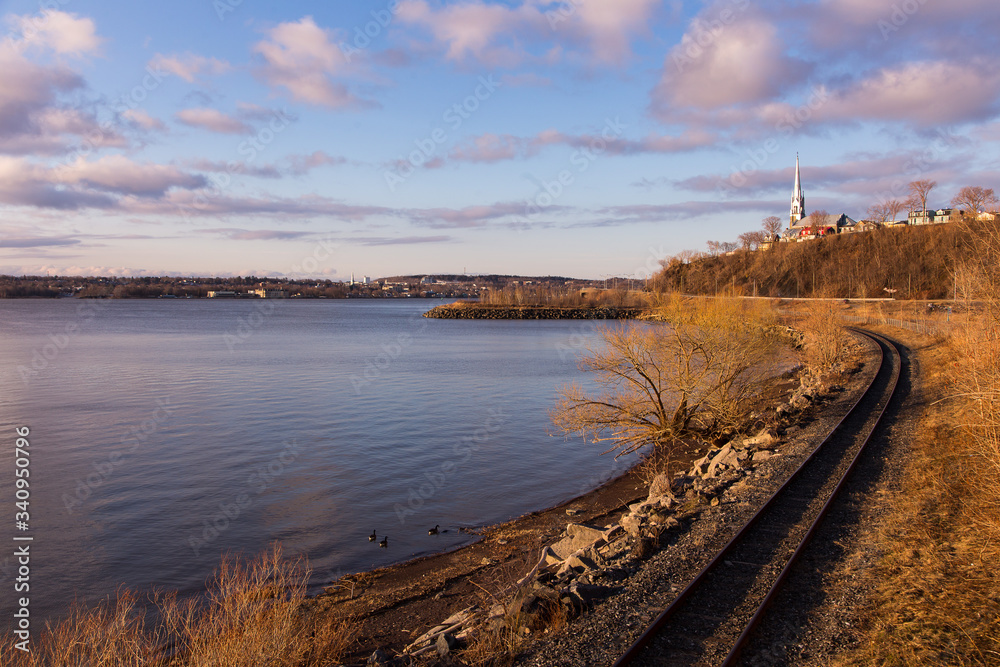 Train track along the St. Michel cove with the Saint-Michel-de-Sillery church dominating a cape in the background seen during a beautiful golden hour spring morning in the Sillery area, Quebec City