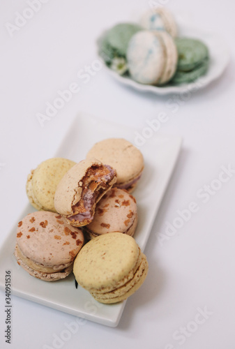 Home made macarons are lying on the white plate on white background with green and white macarons in plate