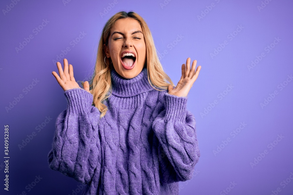 Young beautiful blonde woman wearing casual turtleneck sweater over purple background celebrating mad and crazy for success with arms raised and closed eyes screaming excited. Winner concept Young beautiful blonde woman wearing casual turtleneck sweater over purple background celebrating mad and crazy for success with arms raised and closed eyes screaming excited. Winner concept