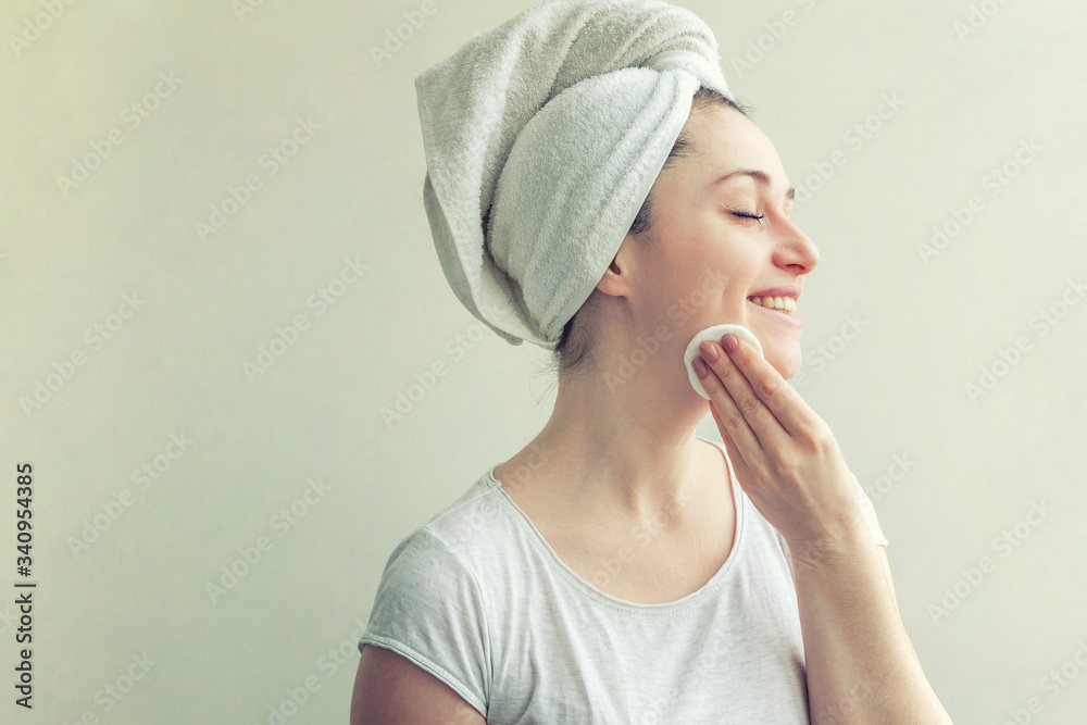 Smiling woman in towel on head with soft healthy skin removing make up with cotton pad isolated on white background Smiling woman in towel on head with soft healthy skin removing make up with cotton pad isolated on white background