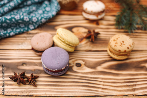 Homemade colorful macaroons are lying on the brown wooden table. Cup of coffee. Anise, honey and colorful tissue.