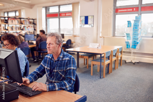 Group Of Mature Adult Students In Class Working At Computers In College Library