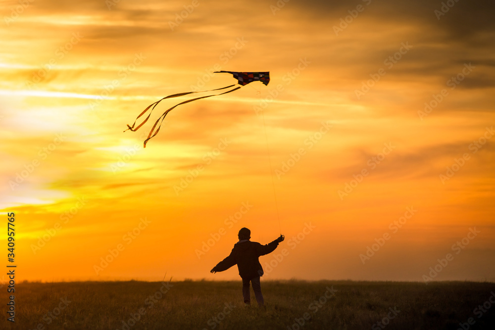 Flying a kite. The boy runs across the field with a kite. Bright, orange sunset. Flying a kite. The boy runs across the field with a kite. Bright, orange sunset.
