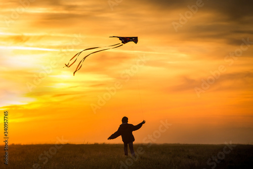 Flying a kite. The boy runs across the field with a kite. Bright, orange sunset.