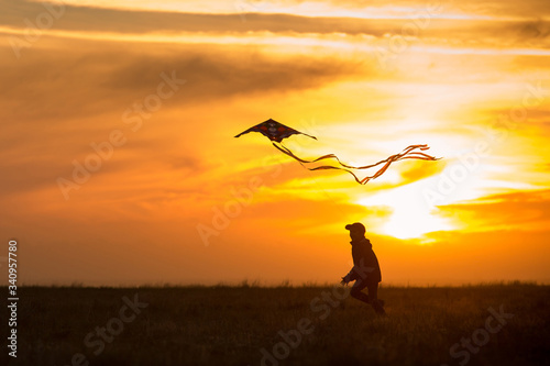 Flying a kite. The boy runs across the field with a kite. Silhouette of a child against the sky. Bright sunset.