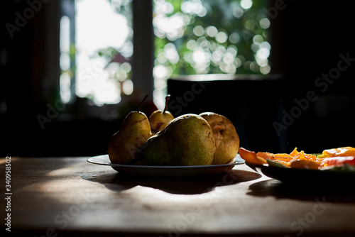 Appetizing pear pham with drops of water on them at home. The white plate with vegetable snack near them in dark key. The sun is shining to the window. photo