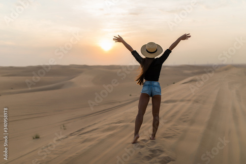 Young sexy woman with straw hat walking barefoot on desert dunes at sunset