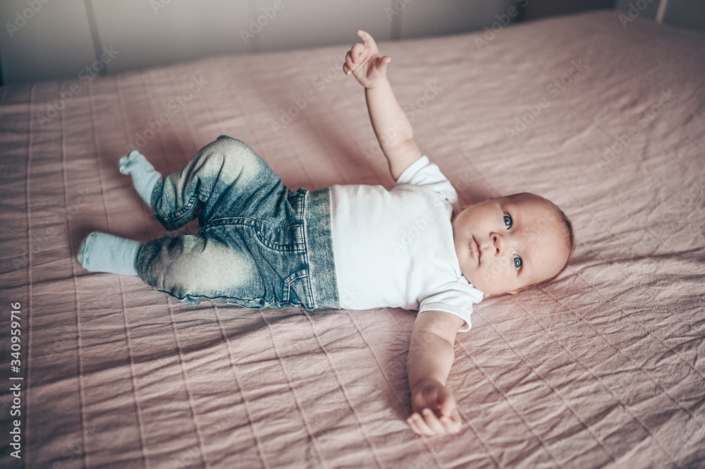 Cute little baby boy lying on pink blanket at bedroom. Newborn. Baby stays  awake on the bed. Closeup portrait of emotional newborn baby in blue jeans  and white t-shirt Stock Photo