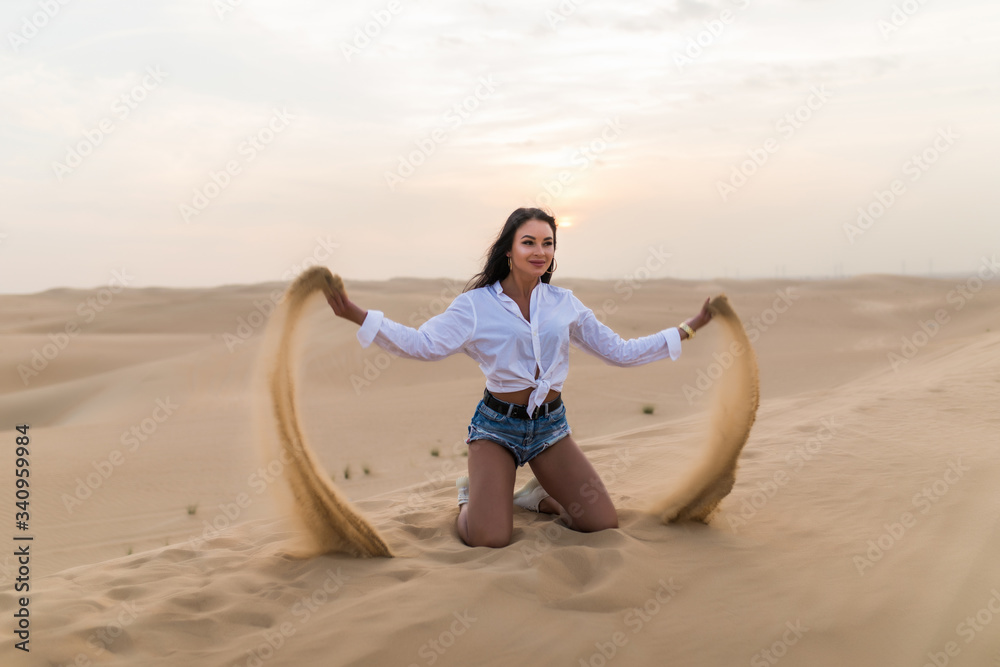 Young sexy woman playing with sand in the dunes desert.