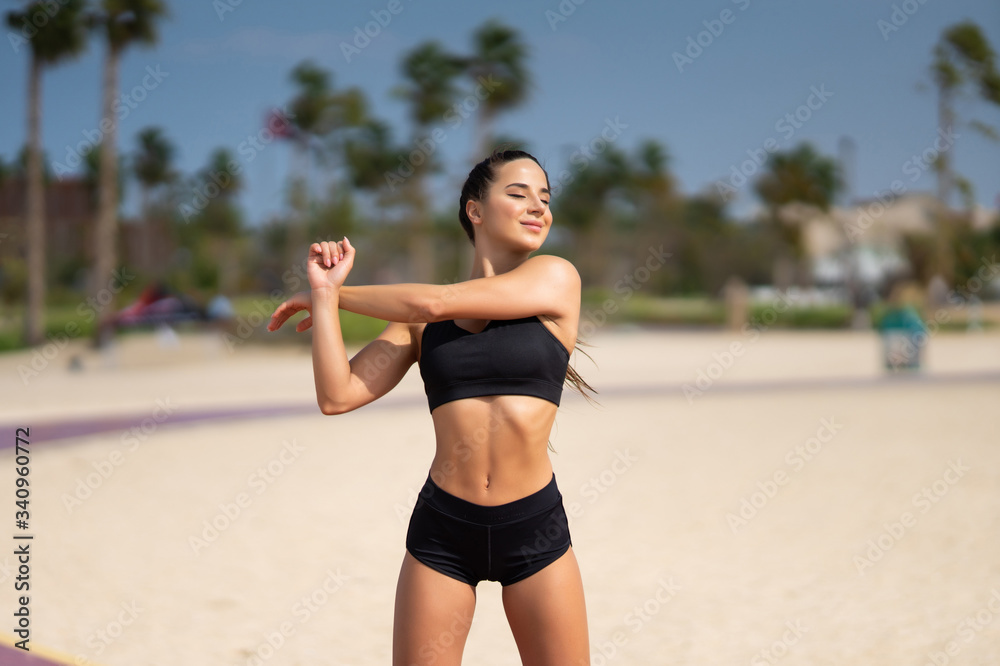 Morning workout. Warming up before training. Young fit woman in sportswear doing hand stretching on the beach at sunrise Morning workout. Warming up before training. Young fit woman in sportswear doing hand stretching on the beach at sunrise
