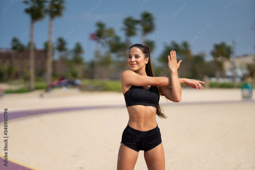 Morning workout. Warming up before training. Young fit woman in sportswear doing hand stretching on the beach at sunrise Morning workout. Warming up before training. Young fit woman in sportswear doing hand stretching on the beach at sunrise