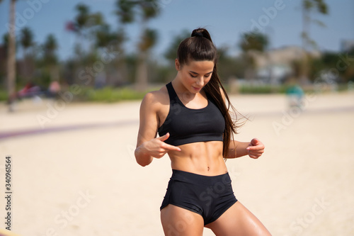 Beautiful fitness woman looking down at her firm stomach and muscular abs results of exercising and training hard in the gym.