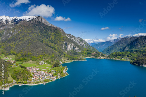 The Improbable aerial landscape of village Molveno  Italy  azure water of lake  empty beach  snow covered mountains Dolomites on background  roof top of chalet  sunny weather  a piers  coastline  