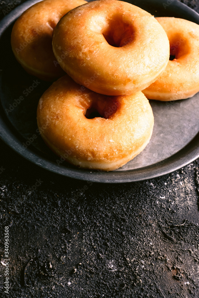 From above heap of yummy fresh doughnuts placed on metal plate on shabby black table From above heap of yummy fresh doughnuts placed on metal plate on shabby black table