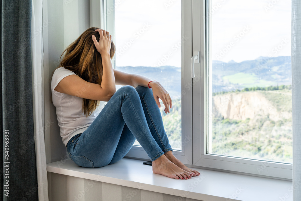 Young woman sitting in the window of her house looks out. Concept of staying at home. Young woman sitting in the window of her house looks out. Concept of staying at home.