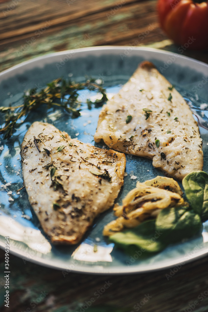 From above roasted fish with basil placed on shabby wooden table near fresh tomatoes and onion From above roasted fish with basil placed on shabby wooden table near fresh tomatoes and onion