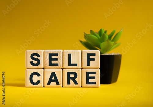 SELF CARE - text on wooden cubes, green plant in black pot on a yellow background photo