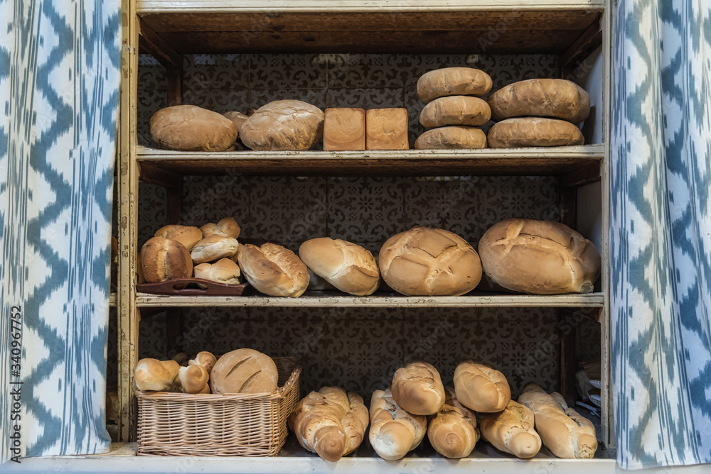 Loaves of assorted fresh bread for sale placed on shabby shelves near curtains in bakery Loaves of assorted fresh bread for sale placed on shabby shelves near curtains in bakery