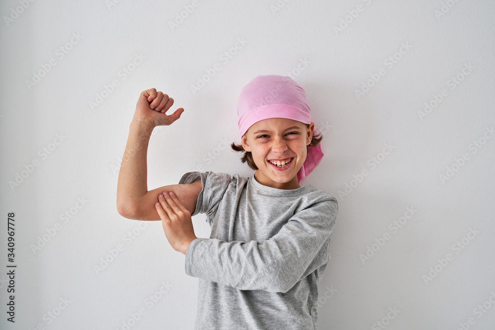 Brave small child with cancer diagnosis looking at camera and screaming while raising fists up on gray background Brave small child with cancer diagnosis looking at camera and screaming while raising fists up on gray background