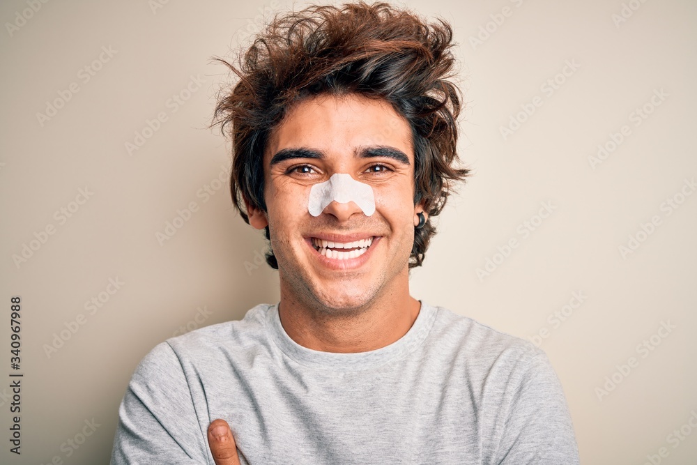 Young handsome man using nose strip standing over isolated white background happy face smiling with crossed arms looking at the camera. Positive person. Young handsome man using nose strip standing over isolated white background happy face smiling with crossed arms looking at the camera. Positive person.
