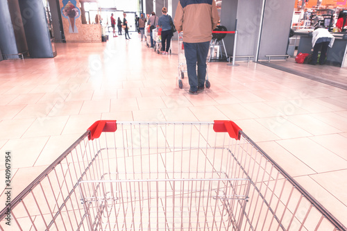 Line at supermarket people respecting social distancing measures  pov from empty shopping cart  - Concept of everyday life in the time of covid-19 pandemic - Image photo