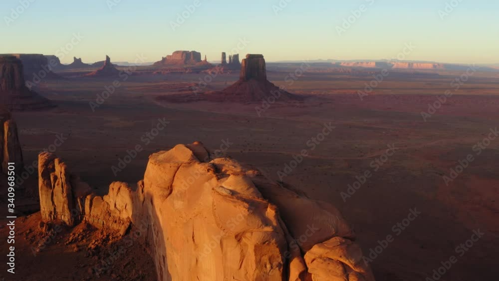Beautiful Panoramic Aerial View of Monument Valley At Sunset, Glowing Canyon Walls in Foreground, Iconic Western Landscape in Background, Tracking Aerial Shot