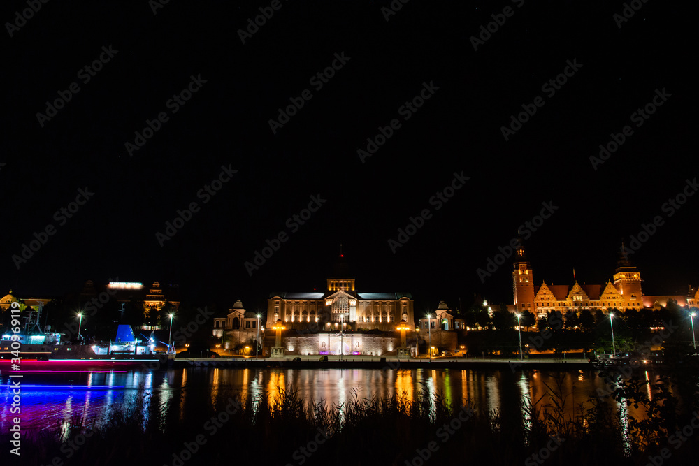 Historic buildings at night. View across the Odra River in Szczecin. Lights of a passing ship