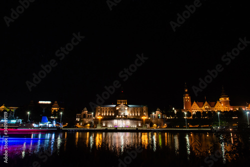 Historic buildings at night. View across the Odra River in Szczecin. Lights of a passing ship