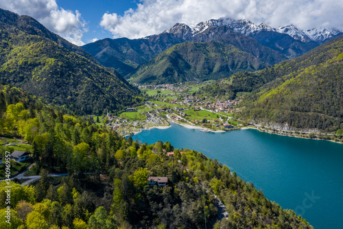 The Improbable aerial landscape of village Molveno  Italy  azure water of lake  empty beach  snow covered mountains Dolomites on background  roof top of chalet  sunny weather  a piers  coastline  