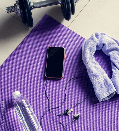 Work out exercise gym items and equipment: dumbbells, mat, water, phone with music. Ready for gym workout. Healthy lifestyle, sport or athlete's equipment on bright mat background. Flat lay. Top view