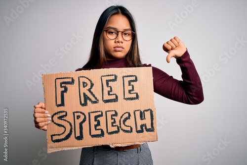Asian girl asking for rights holding banner with free speech message over white background with angry face, negative sign showing dislike with thumbs down, rejection concept