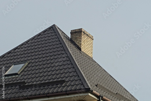 brick chimney on a tiled roof with a window on a background of gray sky