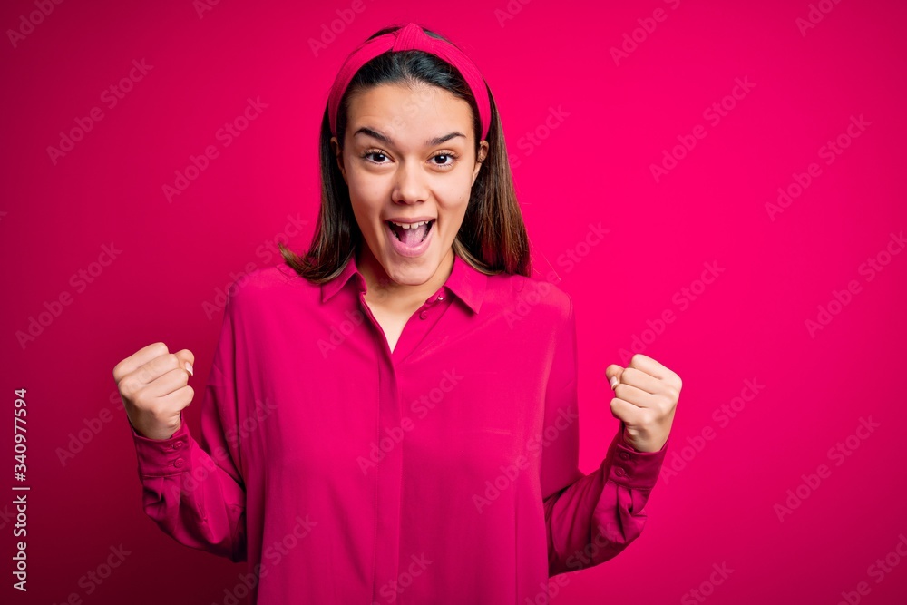 Young beautiful brunette girl wearing casual shirt standing over isolated pink background celebrating surprised and amazed for success with arms raised and open eyes. Winner concept. Young beautiful brunette girl wearing casual shirt standing over isolated pink background celebrating surprised and amazed for success with arms raised and open eyes. Winner concept.