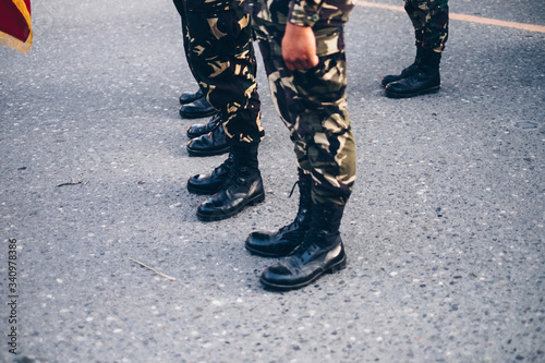 Low section shot of military in camouflage pants and black boots standing on concrete ground. Selective focus. Copy space.