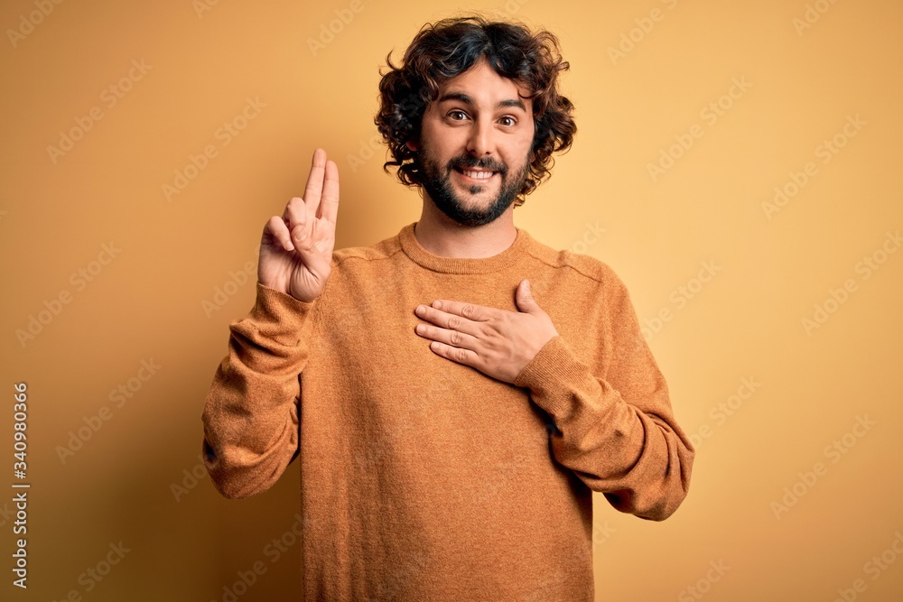 Young handsome man with beard wearing casual sweater standing over yellow background smiling swearing with hand on chest and fingers up, making a loyalty promise oath Young handsome man with beard wearing casual sweater standing over yellow background smiling swearing with hand on chest and fingers up, making a loyalty promise oath