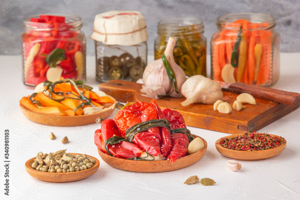 Fermented red hot peppers to enhance immunity with spices on a light wooden table against a background of glass jars with pickled products