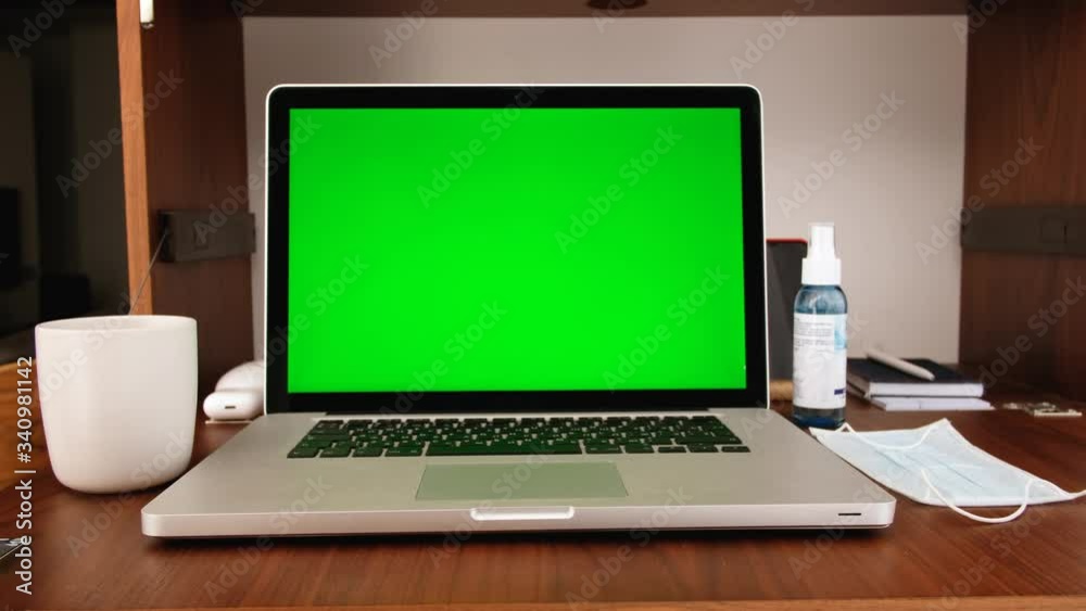 From above keyboard of laptop with green screen while sitting at table with protective mask placed nearby and doing homework during quarantine because of coronavirus From above keyboard of laptop with green screen while sitting at table with protective mask placed nearby and doing homework during quarantine because of coronavirus