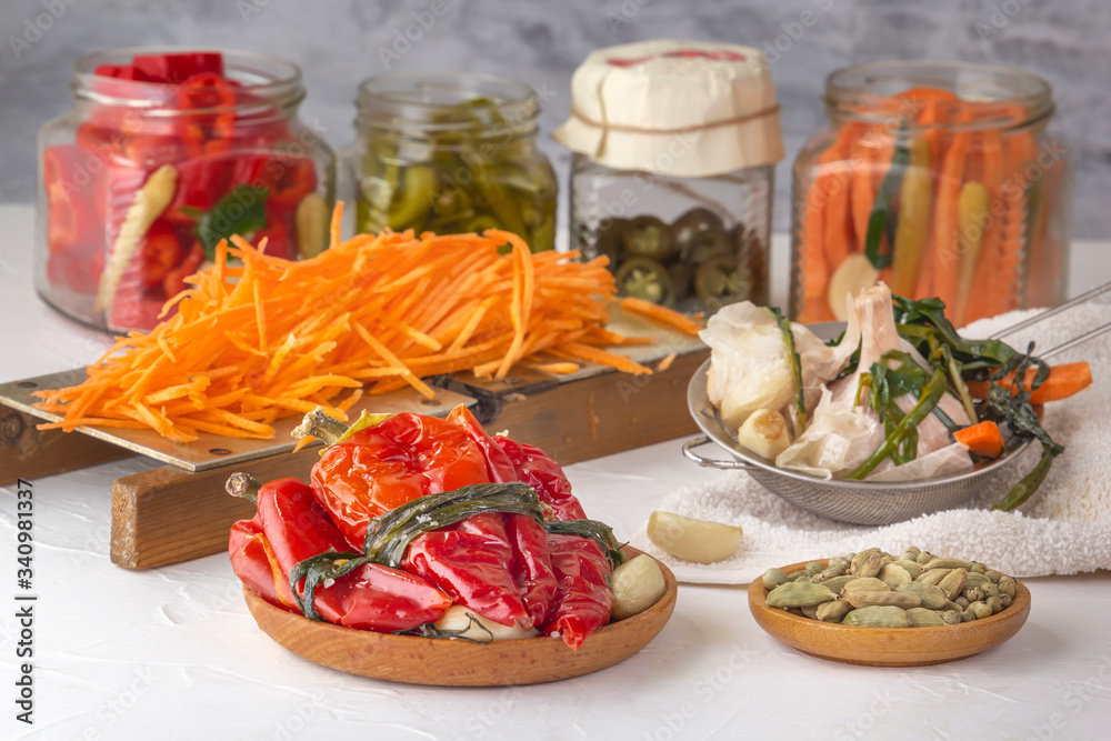 Fermented red hot peppers to enhance immunity with spices and grated carrots on a hand grater on a light wooden table against a background of glass jars with pickled products Fermented red hot peppers to enhance immunity with spices and grated carrots on a hand grater on a light wooden table against a background of glass jars with pickled products