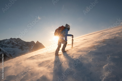 Obraz na plátne Man traveler with tripod are climbing on slope hill on Ryten mount in blizzard a