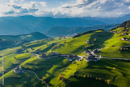 Aerial view of improbable green meadows of Italian Alps  green slopes of the mountains  Bolzano  huge clouds over a valley  roof tops of houses  Dolomites on background  sunshines through clouds