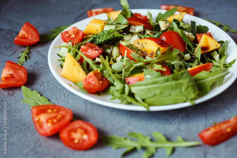 Close up photo of tasty colorful salad made of ruccola, cherry tomatoes, spinach, nectarine, chia seeds. Gray background is decorated with aragua and tomatoes. Close up photo of tasty colorful salad made of ruccola, cherry tomatoes, spinach, nectarine, chia seeds. Gray background is decorated with aragua and tomatoes.